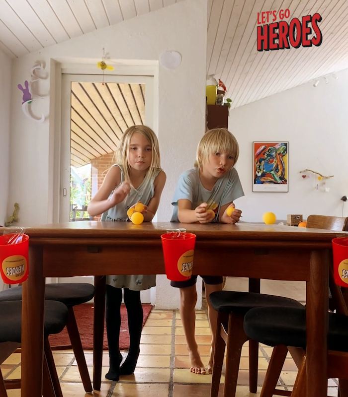 Børn triller bordtennisbolde på spisebord mod plastikkopper.