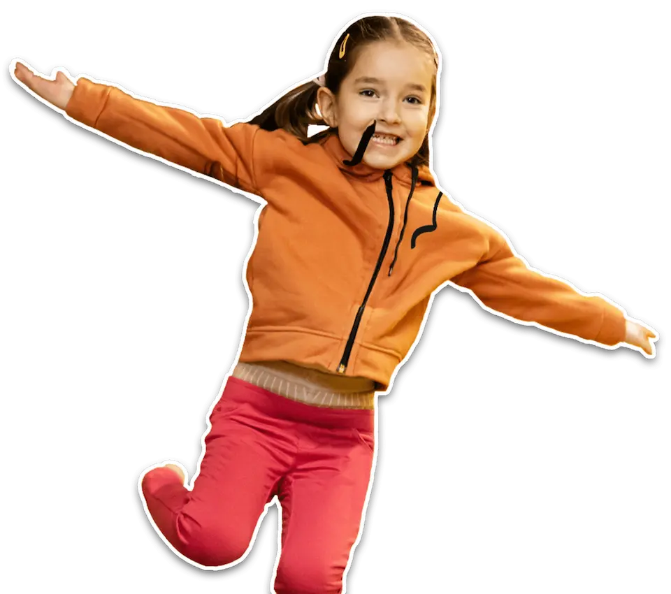 En ung pige i fuld spring, klædt i en orange hættetrøje og røde bukser, med et strålende smil. Hendes dynamiske positur og udstrakte arm symboliserer frihed og glæden ved bevægelse. Billedet fremhæver Let's Go Heroes' engagement i at inspirere børn til at være aktive og lege gennem legende udforskning og eventyr.